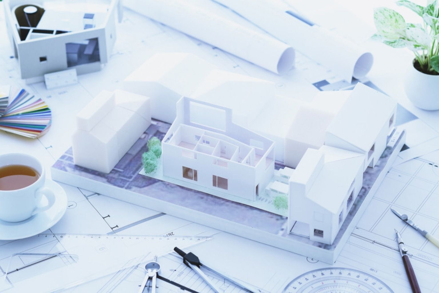 Hvid arkitektmodel af et hus mellem tegninger og ruller